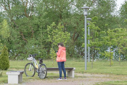 Belarus, Minsk - May 28, 2021: A woman with a bicycle is resting in the park and looks into a smartphone. Stock photography.
