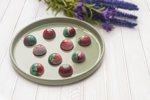 Collectible handmade tempered chocolate candies with a glossy painted body on a round plate with a blurred background and bokeh elements. Stock photography.