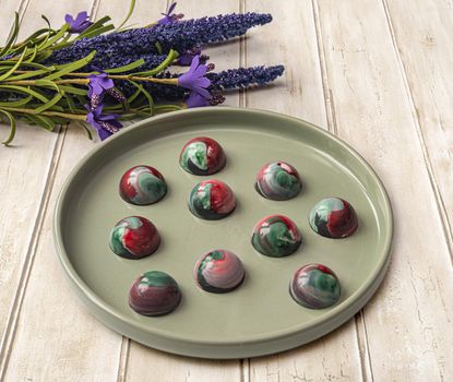 Collectible handmade tempered chocolate sweets with a glossy painted body on a round plate. Stock photography.