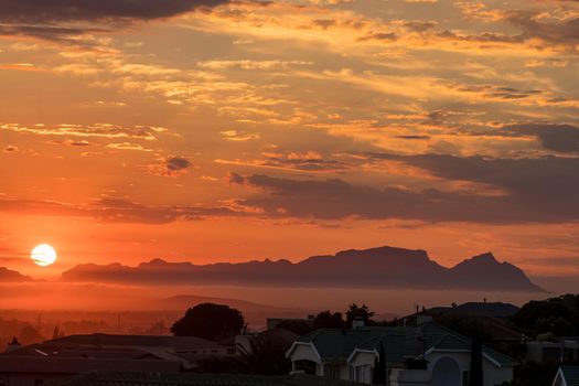 The sun is setting behind Fish Hoek accross False Bay. The back of Table Mountain and Devils Peak are visible