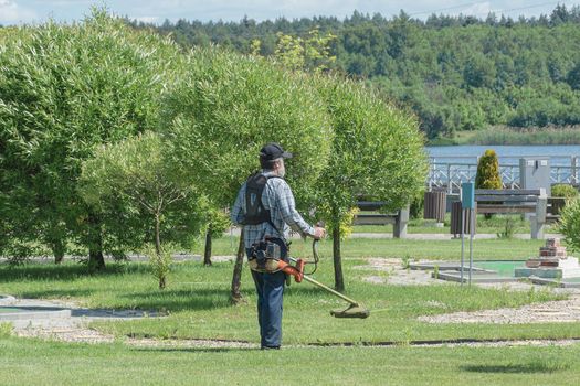 BELARUS, MINSK - JUNE 15, 2021: A man with a hand-held lawn mower mows the grass in a city park. Stock photography.