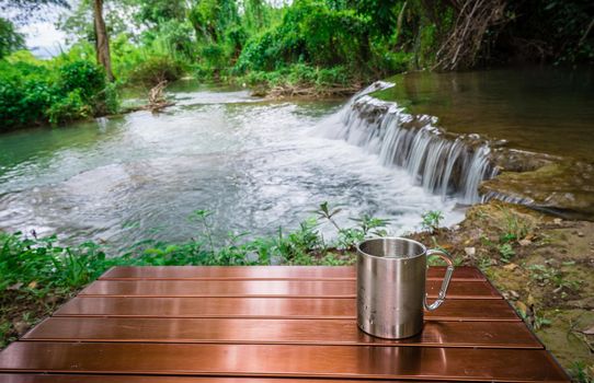 cup of cold drink on the table in front of the waterfall between camping on holiday