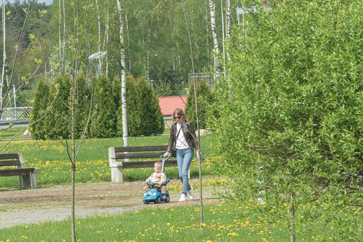Russia, Saratov - May 15, 2021: Mom and child walk along the alley of the park. Stock photography.