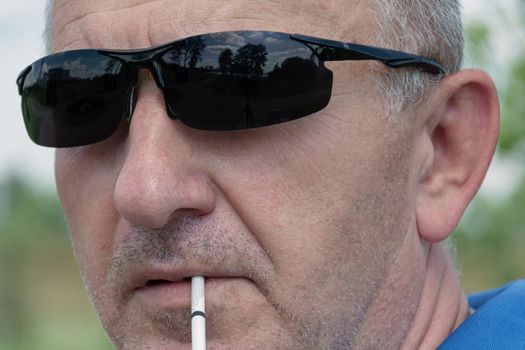 face of a man in dark sunglasses close-up with a cigarette, blurred background with bokeh elements. Stock photography.