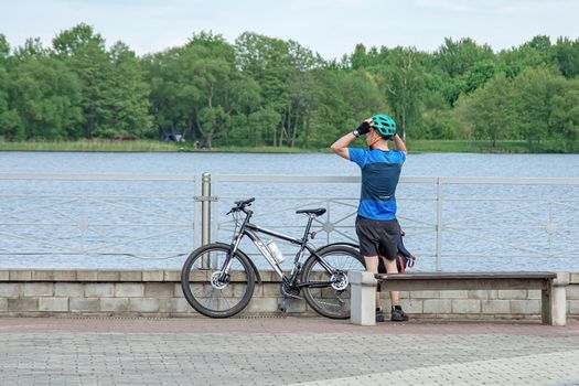 Belarus, Minsk - May 28, 2021: Male cyclist resting on the embankment of the reservoir and looks into the distance at the water. Stock photography.