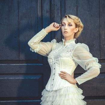 Blonde girl in a retro dress on the background of the old dark door of the building