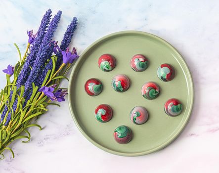 Collectible handmade tempered chocolate sweets with a glossy painted body on a round plate with blur elements. View from above. Stock photography.