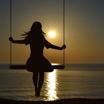 A young woman silhouette who is swinging at the sea shore whaching sunrise