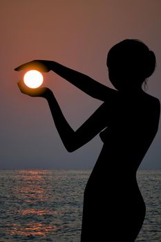 Silhouette of a woman holding the sun in her hands