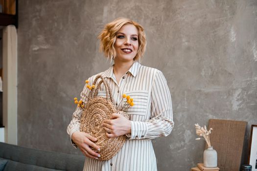Young beautiful stylish woman at home wearing dress, safari style, straw bag