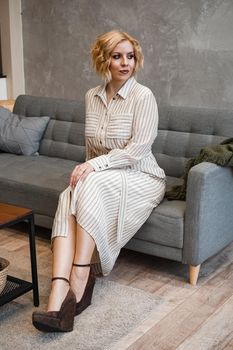 Woman with short blonde hair on sofa in light home room - vertical photo