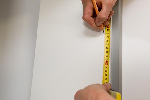 Close up of carpenter hands marks the furniture with a tape measure and a pencil.