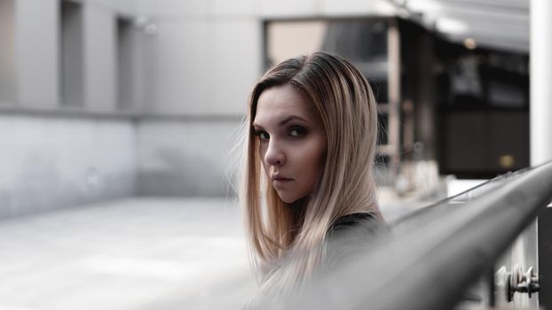 Urban style blonde girl with a stern look standing on the background of a modern building. Wearing black shirt. Girl power and subculture concept.