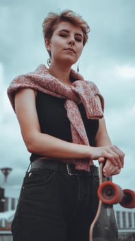 Portrait of young female skateboarder holding her skateboard. Woman with skating board at skate park looking at camera outdoors