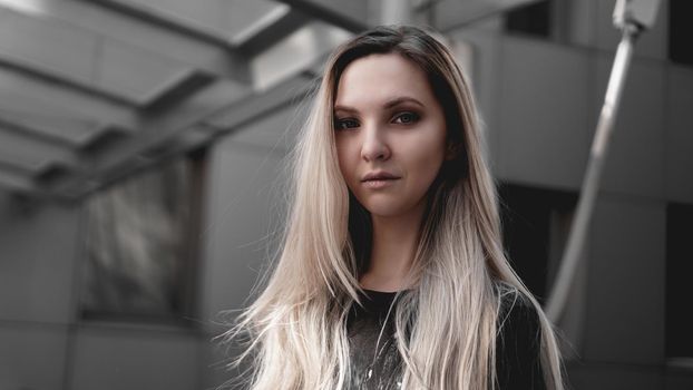 Urban style blonde girl with a stern look standing on the background of a modern building. Wearing black shirt. Girl power and subculture concept.