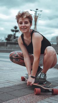 Beautiful young girl with tattoos sits on longboard. She has traditional japanese tattoo