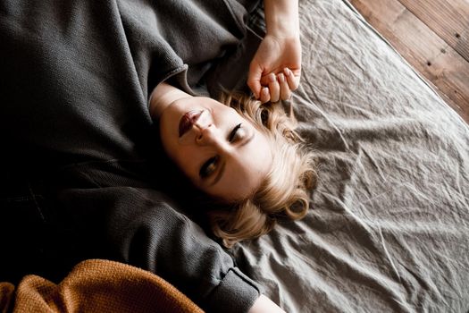 Beautiful young woman with eyes closed in gray sweater lying in bed in her cozy bedroom. Cute girl relaxing at home. Happy morning