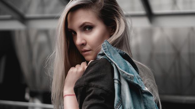 Urban style blonde girl with a stern look standing on the background of a modern building. Wearing black shirt. Girl power and subculture concept.