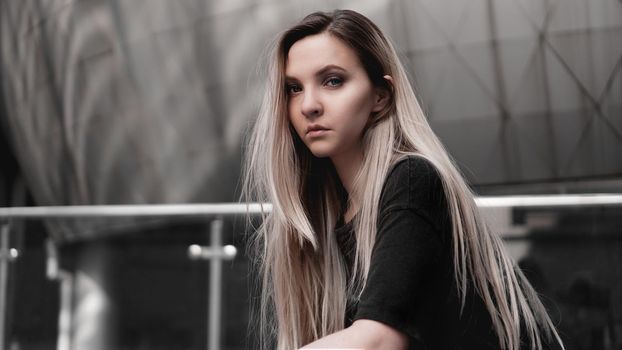 Urban style blonde girl with a stern look standing on the background of a modern building. Wearing black shirt. Girl power and subculture concept.