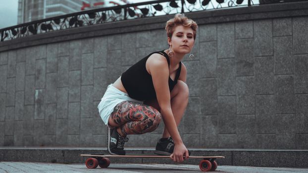 Beautiful young girl with tattoos sits on longboard. She has traditional japanese tattoo