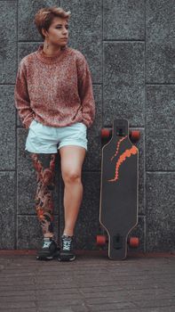 Beautiful young girl with tattoos with longboard in the town. She has traditional japanese tattoo