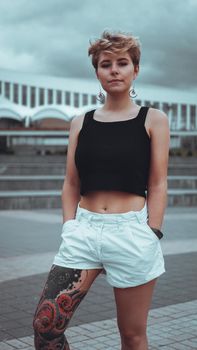 Young woman with trendy short blonde hair outdoor portrait at city with japanese tattoo