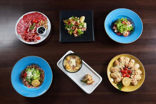 Food heaven. Top view of a restaurant table with plates of salads bowl of soup assorted cold meet appetizers and shellfish mussels baked with cheese