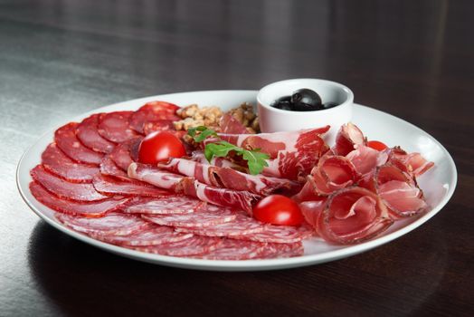 Meat deli. Assorted salami and ham plate decorated with cherry tomatoes black olives and walnuts