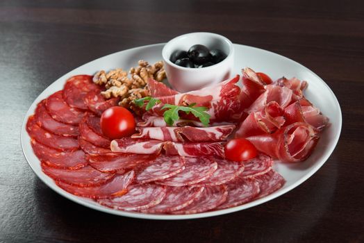 For meat lovers. Closeup of a cold meat appetizers served on a plate with black olives and walnuts at the restaurant table