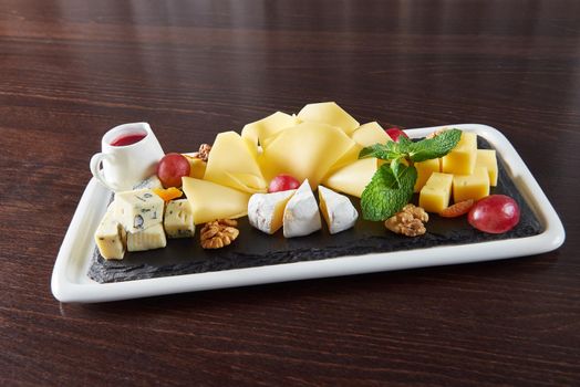 Cheese love. Cheese plate with Dorblu Brie Gouda and Camembert on a plate served with walnuts and grapes on a restaurant table