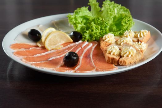 Classic appetizer. Closeup of a sliced smoked salmon served with green salad leaves black olives and slices of bread with butter