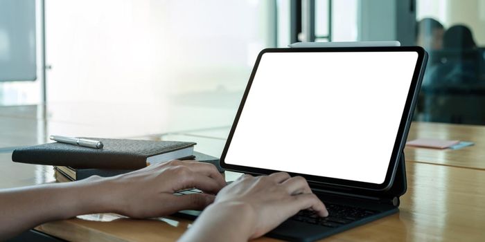 Mockup image of business woman using and typing on laptop with blank white screen and coffee cup on glass table in modern loft cafe.