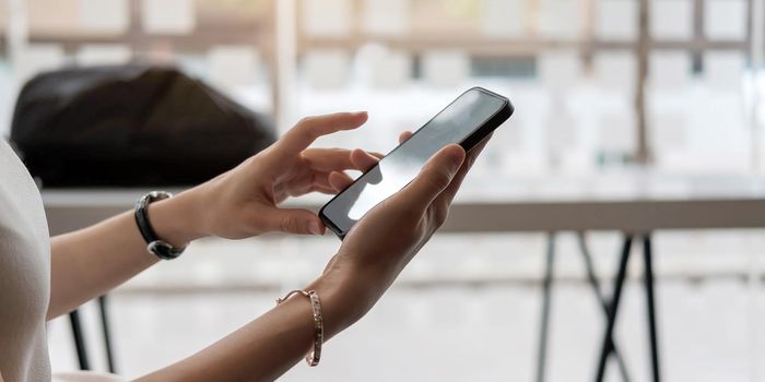 Mockup image blank white screen cell phone.women hand holding texting using mobile on desk at home office..