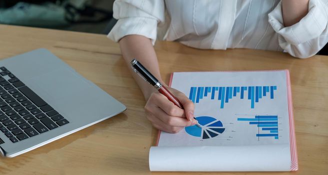 Close up of businessman or accountant hand holding pen working on calculator to calculate business data, accountancy document and laptop computer at office, business concept..