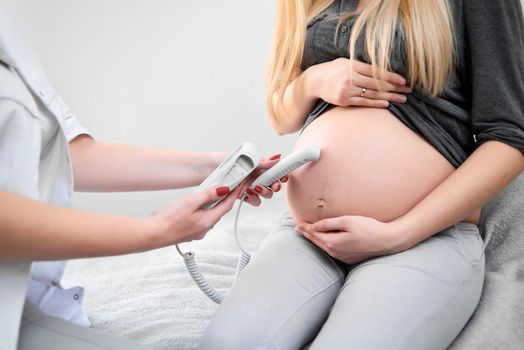 Cropped close up of a doctor examining belly of her pregnant patient at the clinic pregnancy family planning mother children babies expecting unborn equipment scanning measuring health concept.