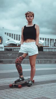 Beautiful young girl with tattoos with longboard in the town. She has traditional japanese tattoo