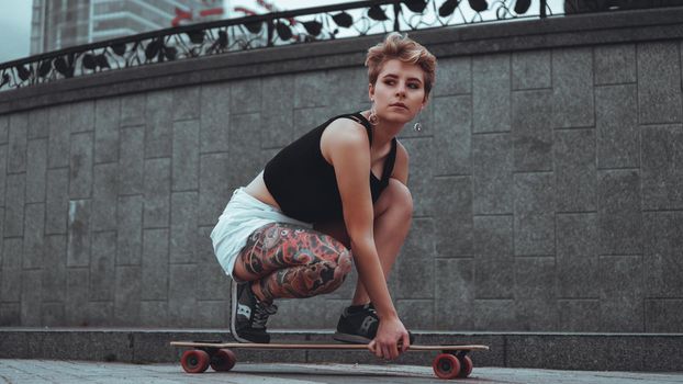 Beautiful young girl with tattoos sits on longboard. She has traditional japanese tattoo