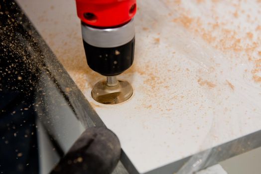 Drilling a hole for a hinge on a furniture door. Selective focus. Close up.