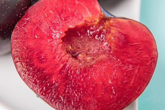 On a white saucer is a large plum, cut in half, and next to it is a whole plum. The pulp of red berries. Close-up.