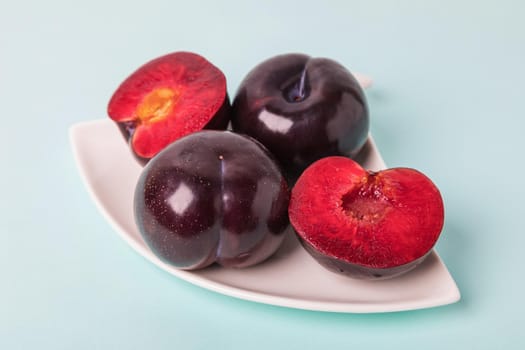 On a white saucer is a large plum, cut in half, and next to it is a whole plum. The pulp of red berries. Close-up.