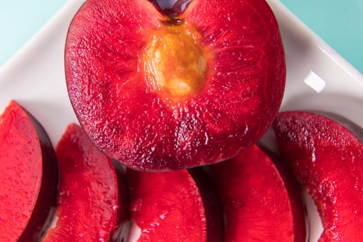 On a white saucer, a large plum, cut in half, with slices next to it. The pulp of red berries. Close-up.