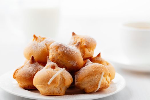 Morning coffee with cakes. Profiteroles, coffee, cream on a white wooden table.