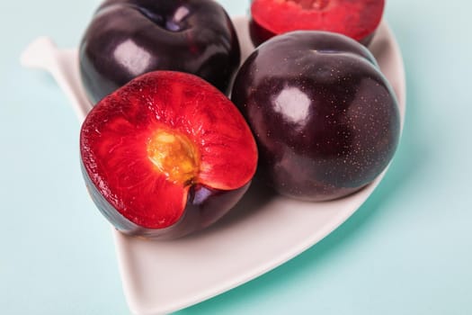 On a white saucer is a large plum, cut in half, and next to it is a whole plum. The pulp of red berries. Close-up.