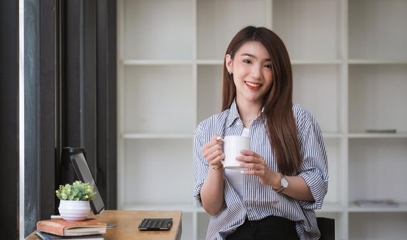 Asian woman drinking coffee and relax in coffee shop cafe. Beautiful female looking at camera during working with digital tablet.