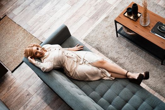 Top view of a smiling young woman relaxing on sofa at weekend an home