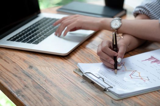 Close up accountant analyst holding documents working with laptop computer doing online trade market tech research thinking working sit at home office desk