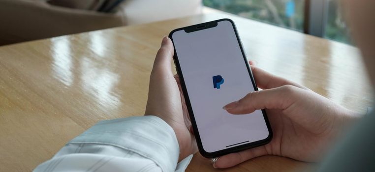 CHIANG MAI, THAILAND - JUL 24, 2020 : Woman hands holding iphone Xs with PayPal apps on the screen. PayPal is an online electronic payment system..