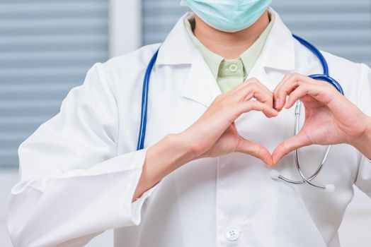 Closeup of doctor woman wearing white coat standing making heart finger shape, Doctor's hand sign, Healthy medical heart coronavirus concept