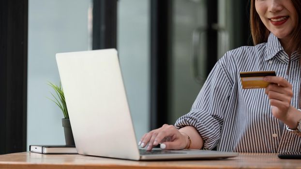 Happy asian woman buying online with laptop computer and credit card at home.