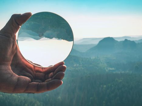 Stunning landscape of the Saxony National Park in Germany reflecting in a large glass ball in male hand fingers